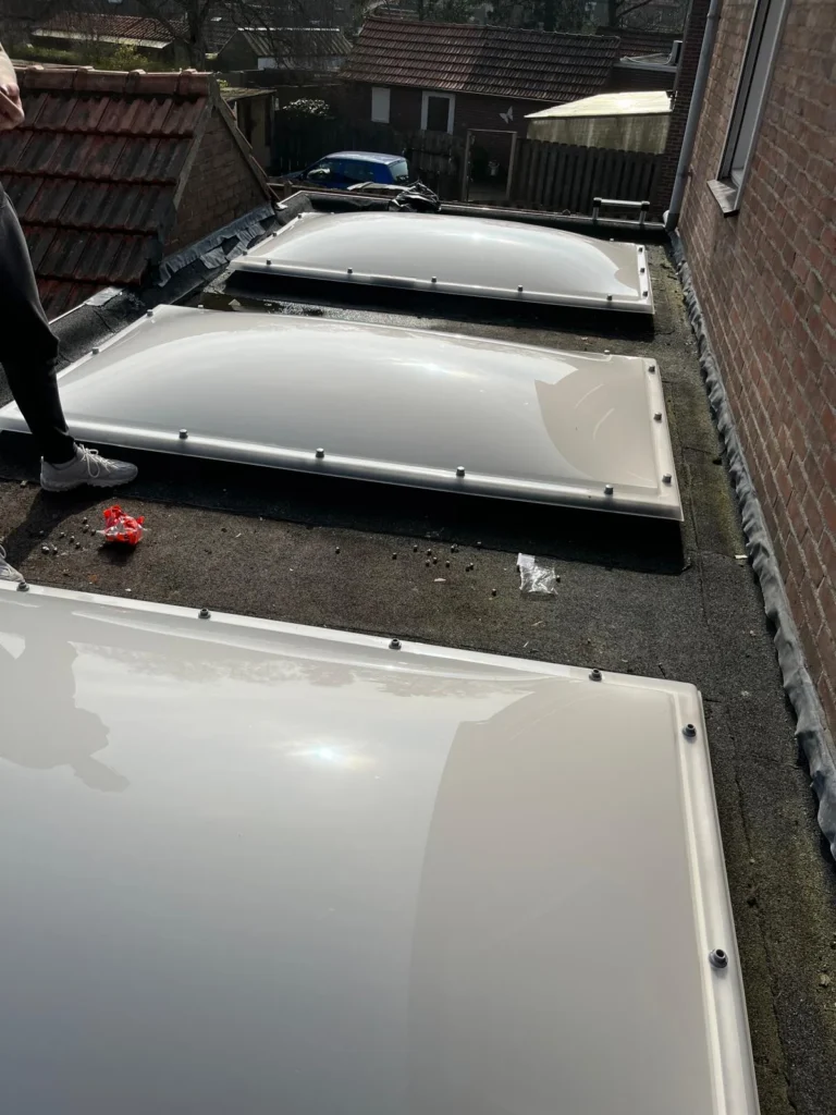 Drie lichtkoepels op een plat dak tussen rijtjeswoningen in Lunteren