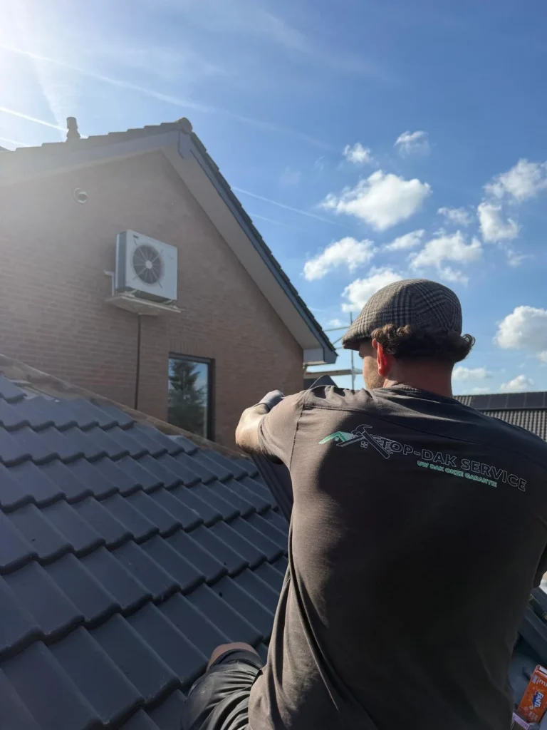 Dakdekker met pet werkt op een pannendak naast een woning in Lunteren