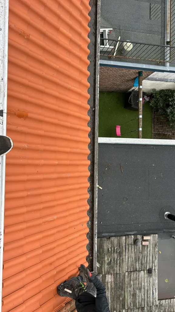 Dakgoot tussen een oranje pannendak en een plat dak van bovenaf in Lunteren